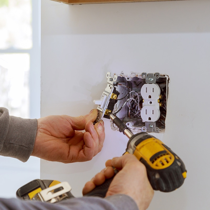Installation d'un interrupteur et d'une prise électrique murale. Main utilise perceuse pour connexion dans boîte.